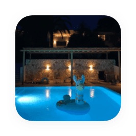 La piscine privée éclairée la nuit, avec le mur en pierre de la villa et les lumières du jardin derrière.
